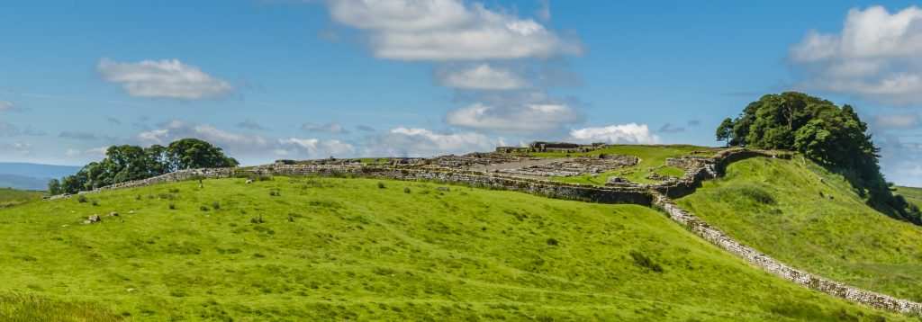 Trail running along Hadrian's Wall Path, Hadrian's Wall stretching across a green field